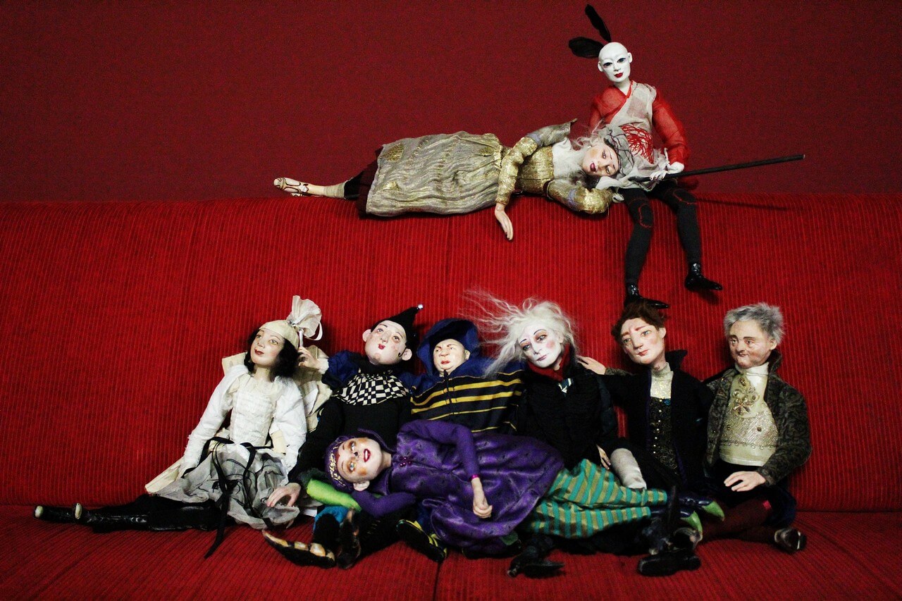 Zdjęcie do spektaklu spiąca Królewna. Pokazuje wszsytkie lalki wystepujące w spektaklu siedzące na czerwonej kanapie.
