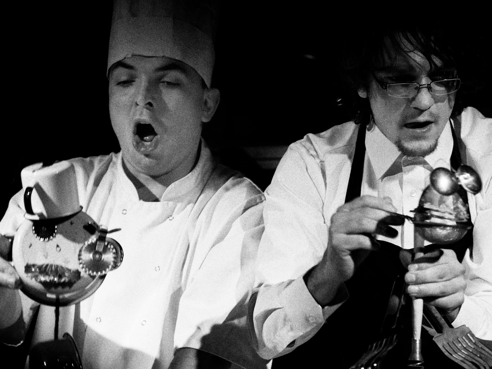 Zdjęcie ze spektaklu Wielkie Ciasto. Przedstawia dwóch aktorów przebranych za kucharzy animujących lalki zrobione z garnków.