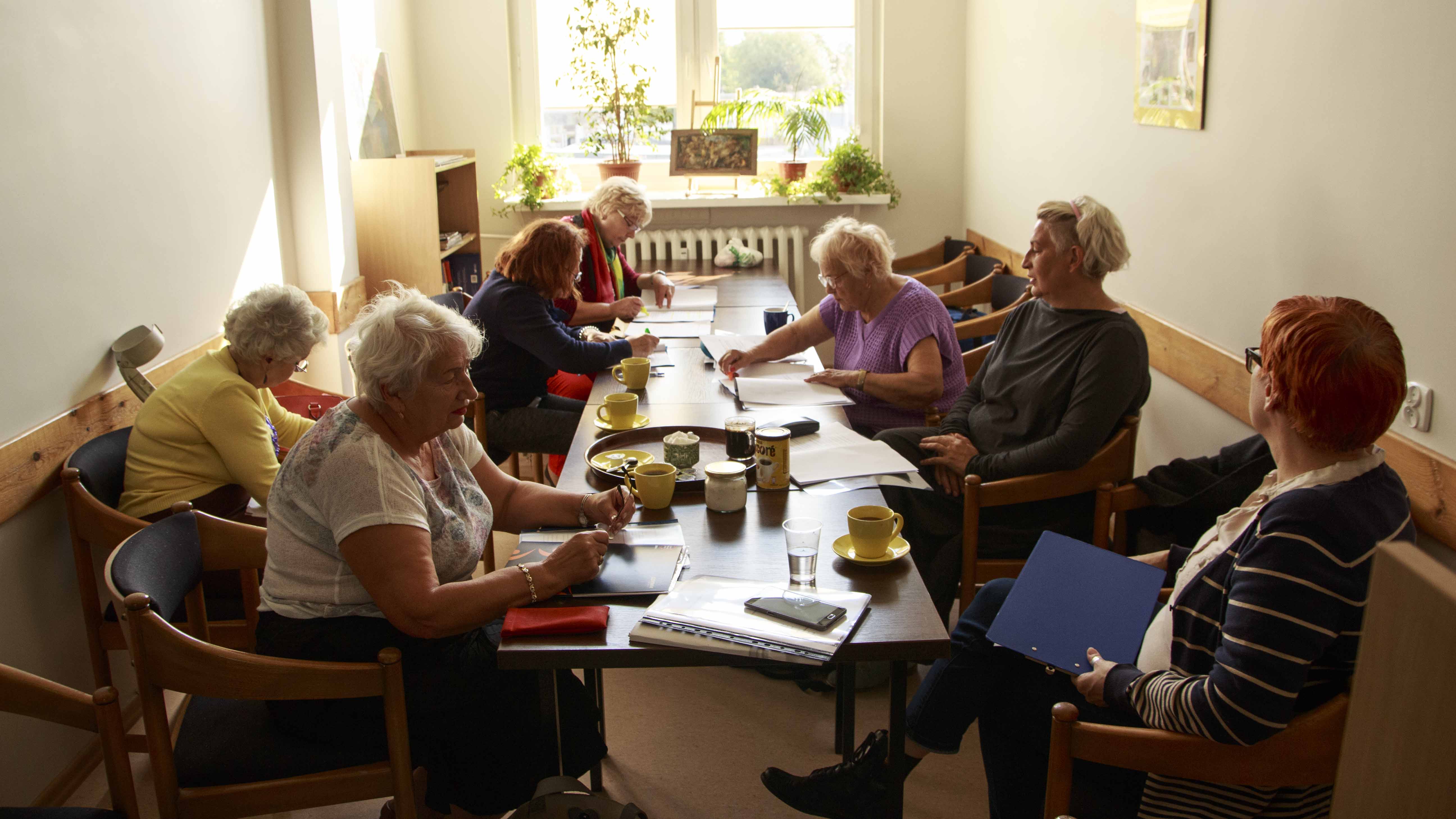 Zdjęcie z projektu Chór dzielnicowy. Kilka starszych kobiet przy stole podczas próby, pochylonych nad scenariuszami.