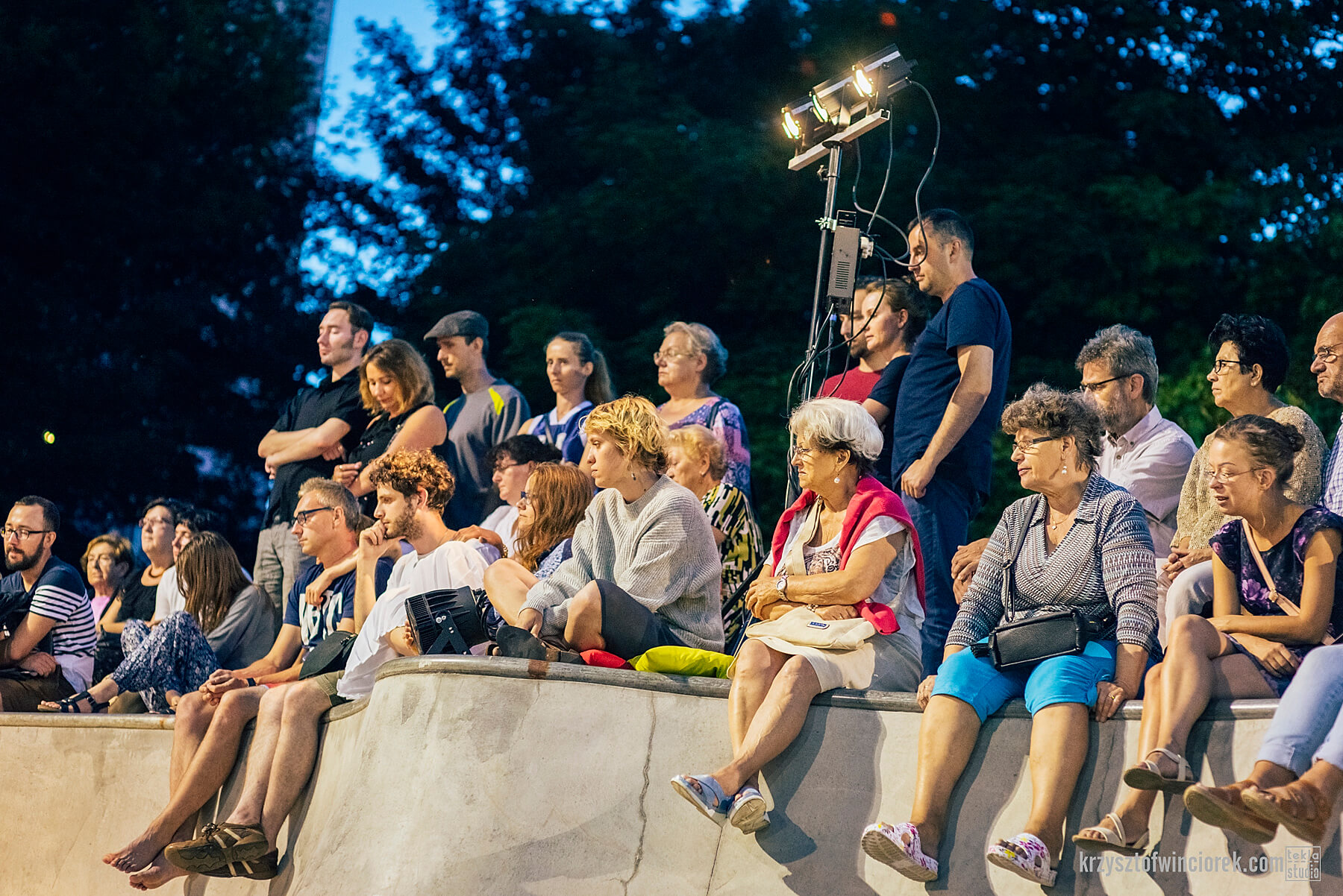 zdjęcie widzów spektaklu siedzących na rampie w skate parku, wieczorem