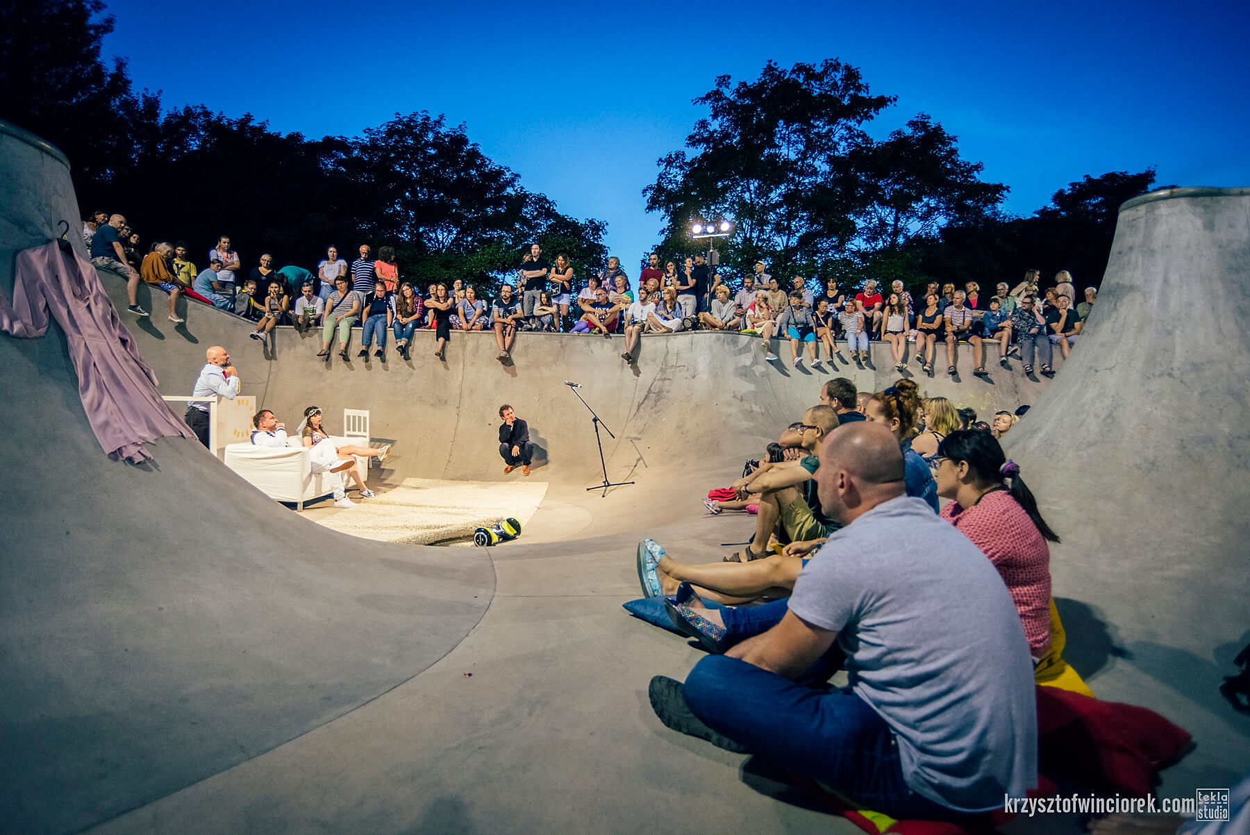 zdjęcie widzów spektaklu siedzących na rampie w skate parku, wieczorem