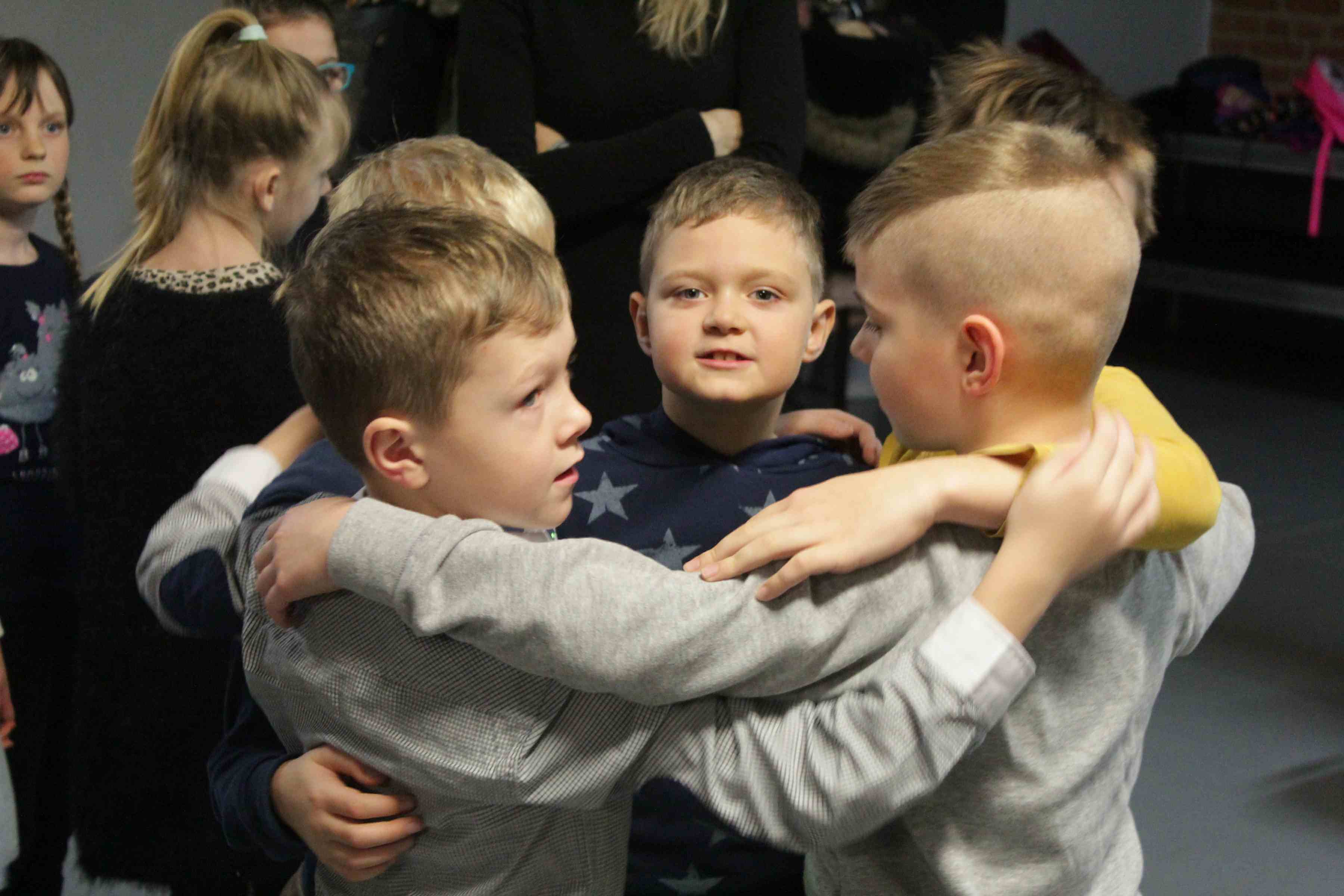 pięcioro chłopców stoi w kółku trzymając się za ramiona, za nimi widać inne dzieci oraz ich opiekunkę