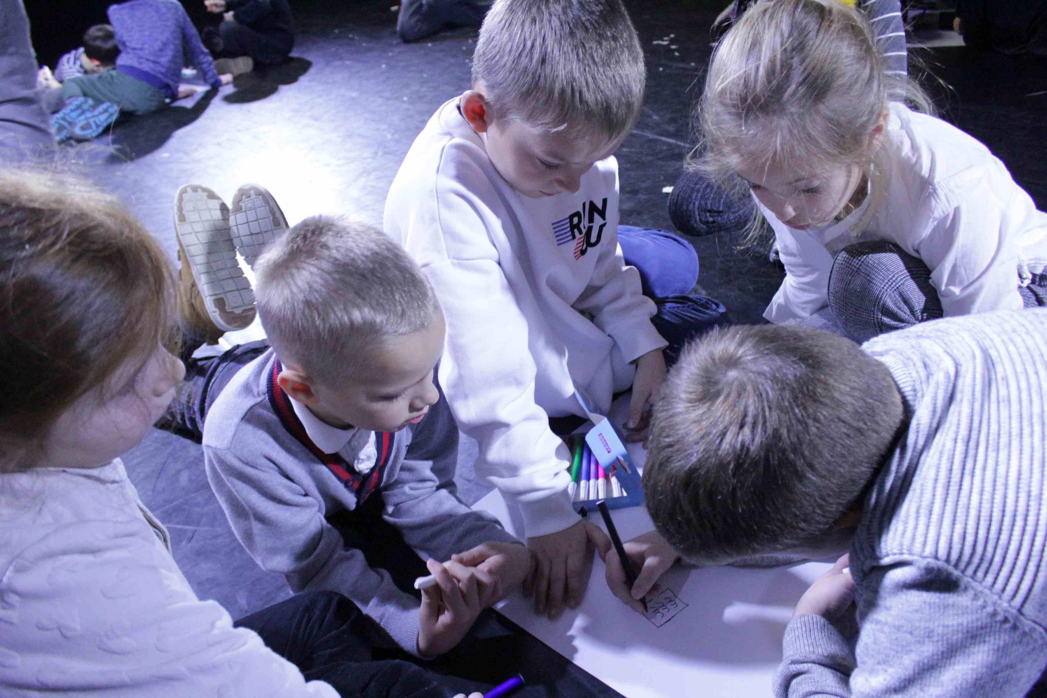 grupa dzieci pracujących nad pracą plastyczną, w dłoniach mają kolorowe flamastry
