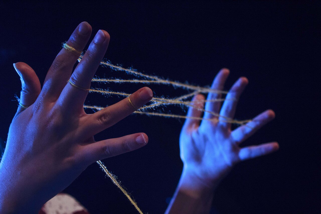 zbliżenie na dłonie wokół palców których zaplątany jest żółty sznurek, pana niebieskie światło, zdjęcie z akcji W SIECI - miejska akcja Teatru Gdynia Główna w przestrzeni Dworca PKP