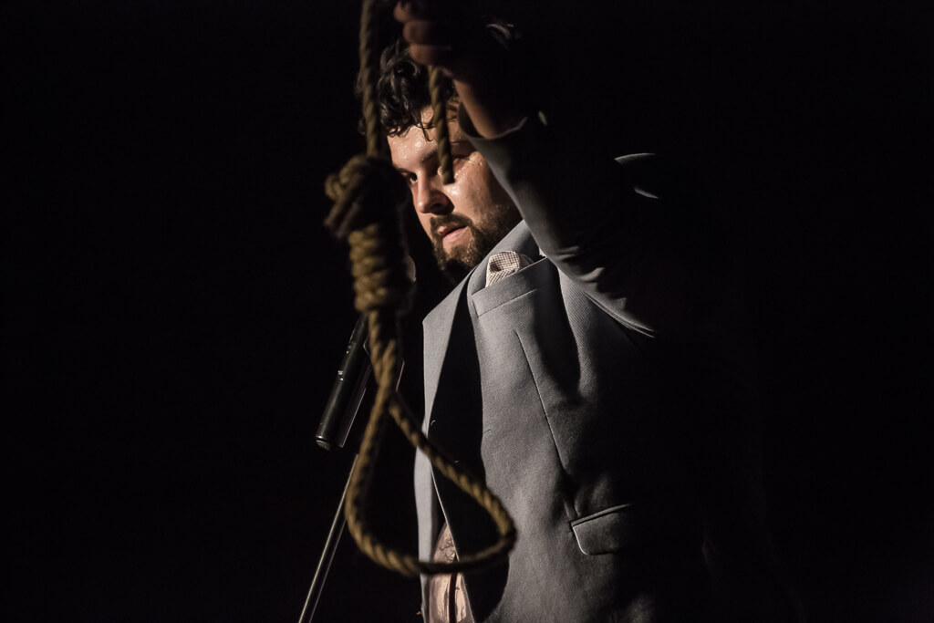 Zdjęcie do spektaklu KAZANIE XXI. Na zdjęciu znajduje się aktor trzymający w ręce pętlę ze sznura.