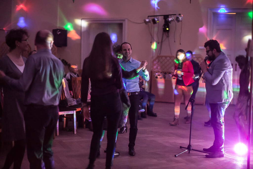Zdjęcie do spektaklu KAZANIE XXI. Na zdjęciu widać tańczących ludzi w akompaniamencie kolorowych świateł i śpiewu piosenkarza stojącego przy mikrofonie.