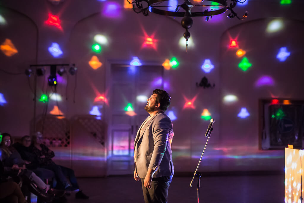 Zdjęcie do spektaklu KAZANIE XXI. Na zdjęciu widać aktora stojącego na środku sali, patrzącego w przyozdobiony kolorowymi światłami sufit.