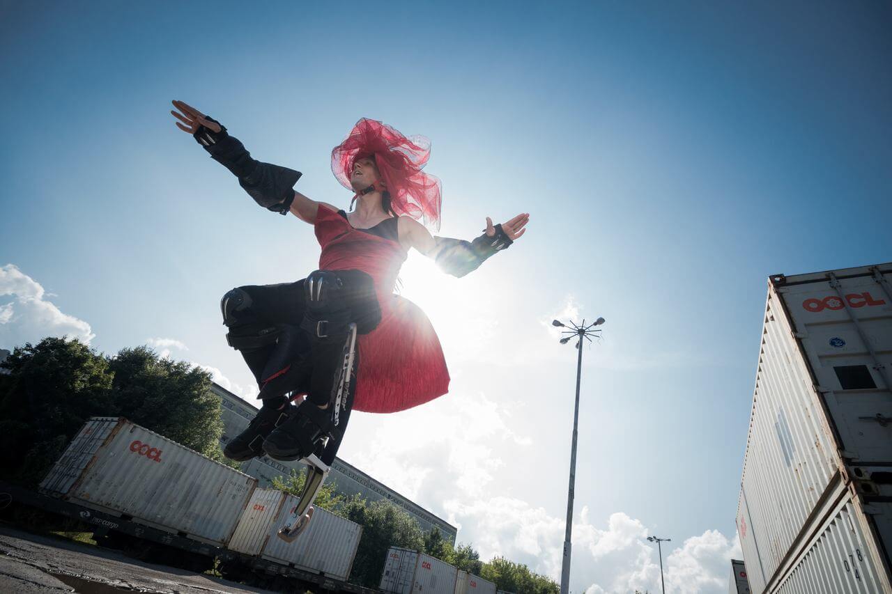 Zdjęcie do spektaklu Masska. Aktor w czerwono czarnym kostiumie skacze na platformie.