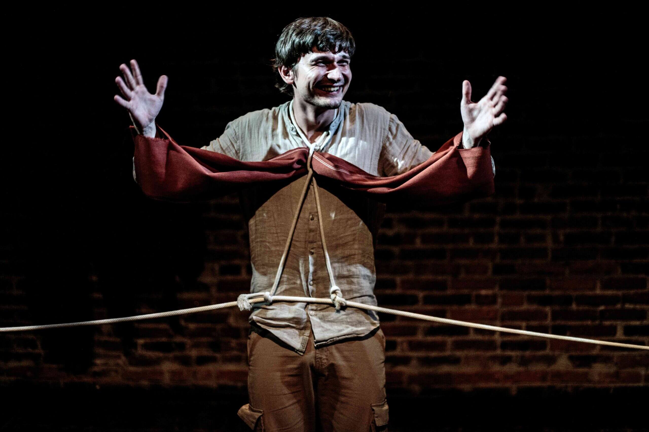 zdjęcie przedstawia aktora z uniesionymi rekami i przewiązanego w pasie liną