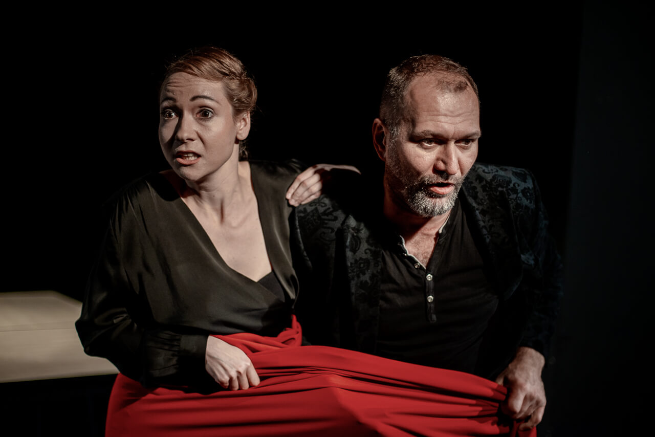 Na zdjęciu dwoje aktorów, kobieta i mężczyzna zawinięci w czerwony materiał