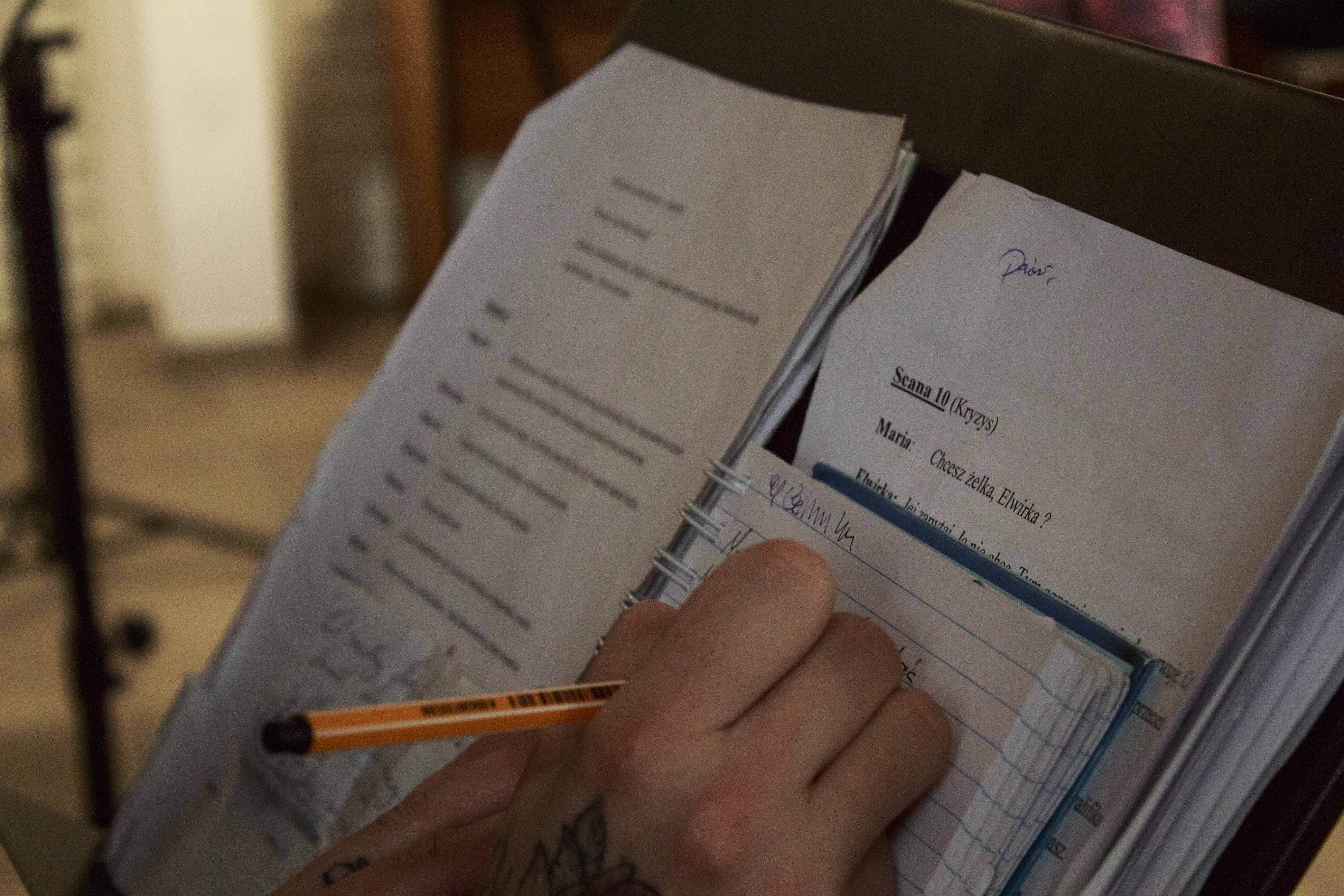 Zdjęcie scenariusza na pulpicie. widać też dłoń z długopisem.
