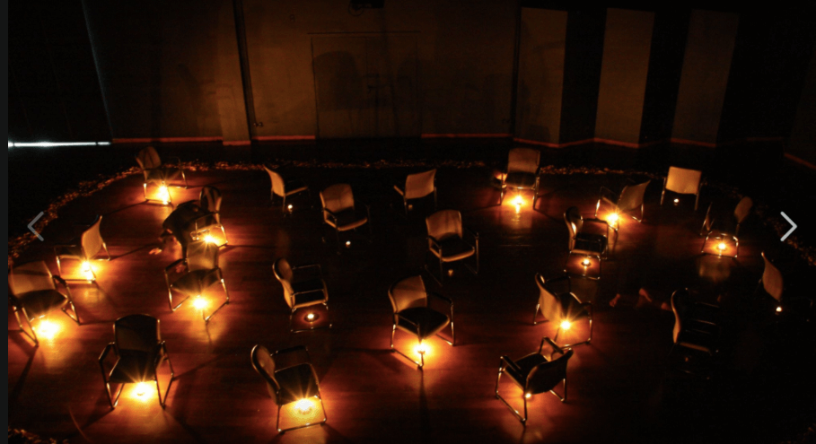 Scena pokazana z lotu ptaka. Na scenie chaotycznie rozstawione krzesła, podświetlone od dołu światełkami lampionów.