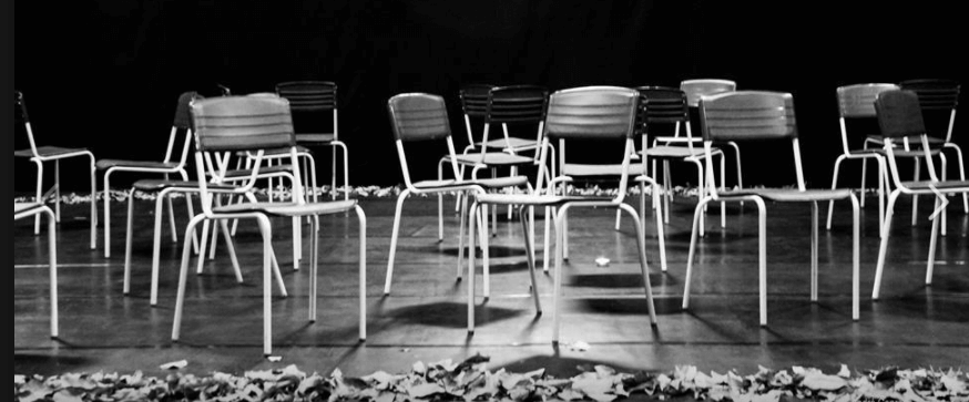 Czarno-białe zdjęcie z Festiwalu Between.Pomiędzy 2018. Chaotycznie rozstawione na scenie krzesła, pod którymi ułożone są lampiony.