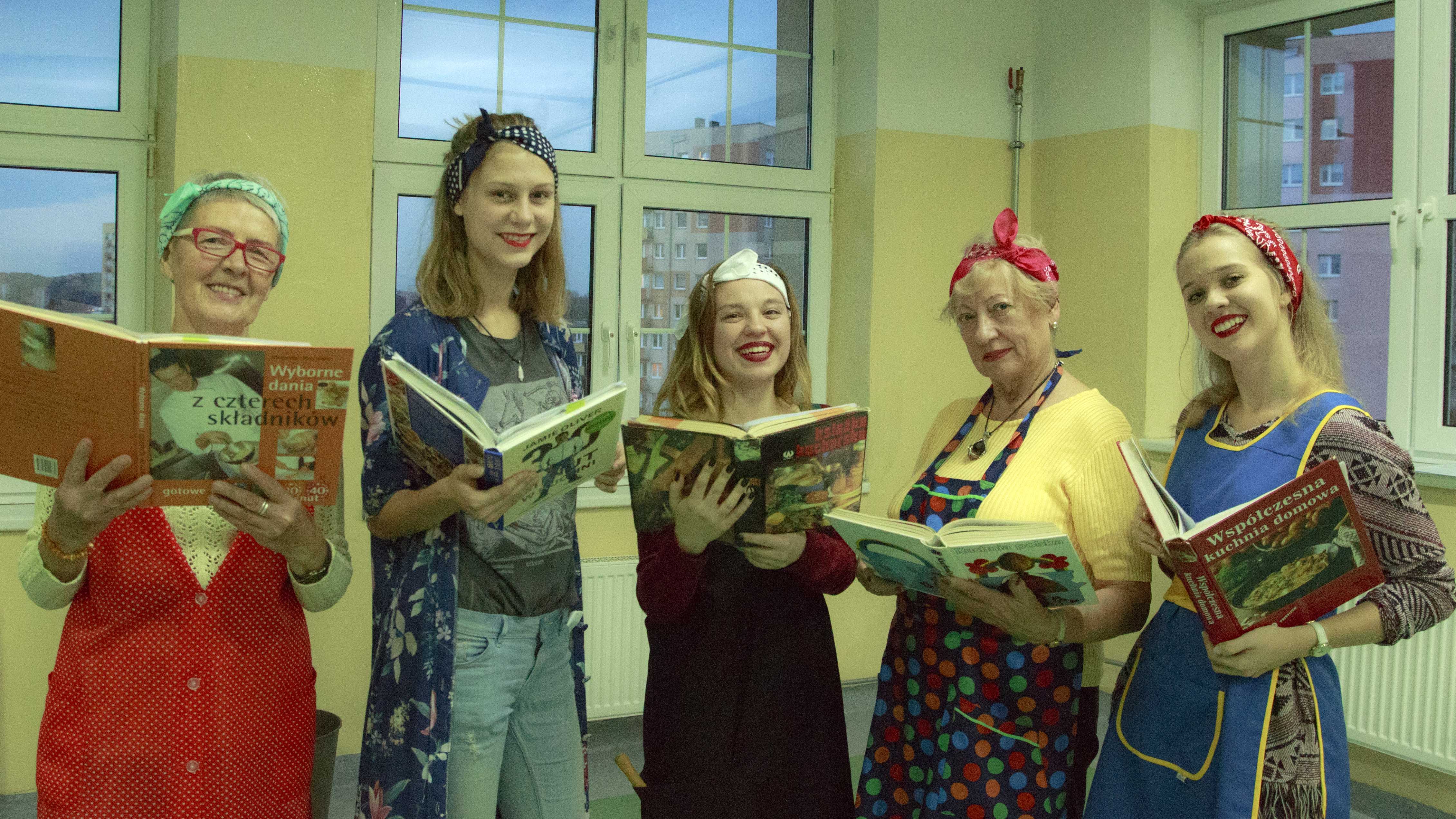 zdjęcie z projektu Dzwięczące wieżowce. Pięć aktorek w fartuchach kuchennych trzymających przed sobą książki kucharskie.