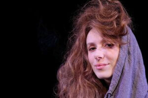 Zdjęcie portretowe. na zdjęciu twarz kobiety, ciasny kadr, na głowie kaptur, widać długie włosy i uśmiechniętą twarz