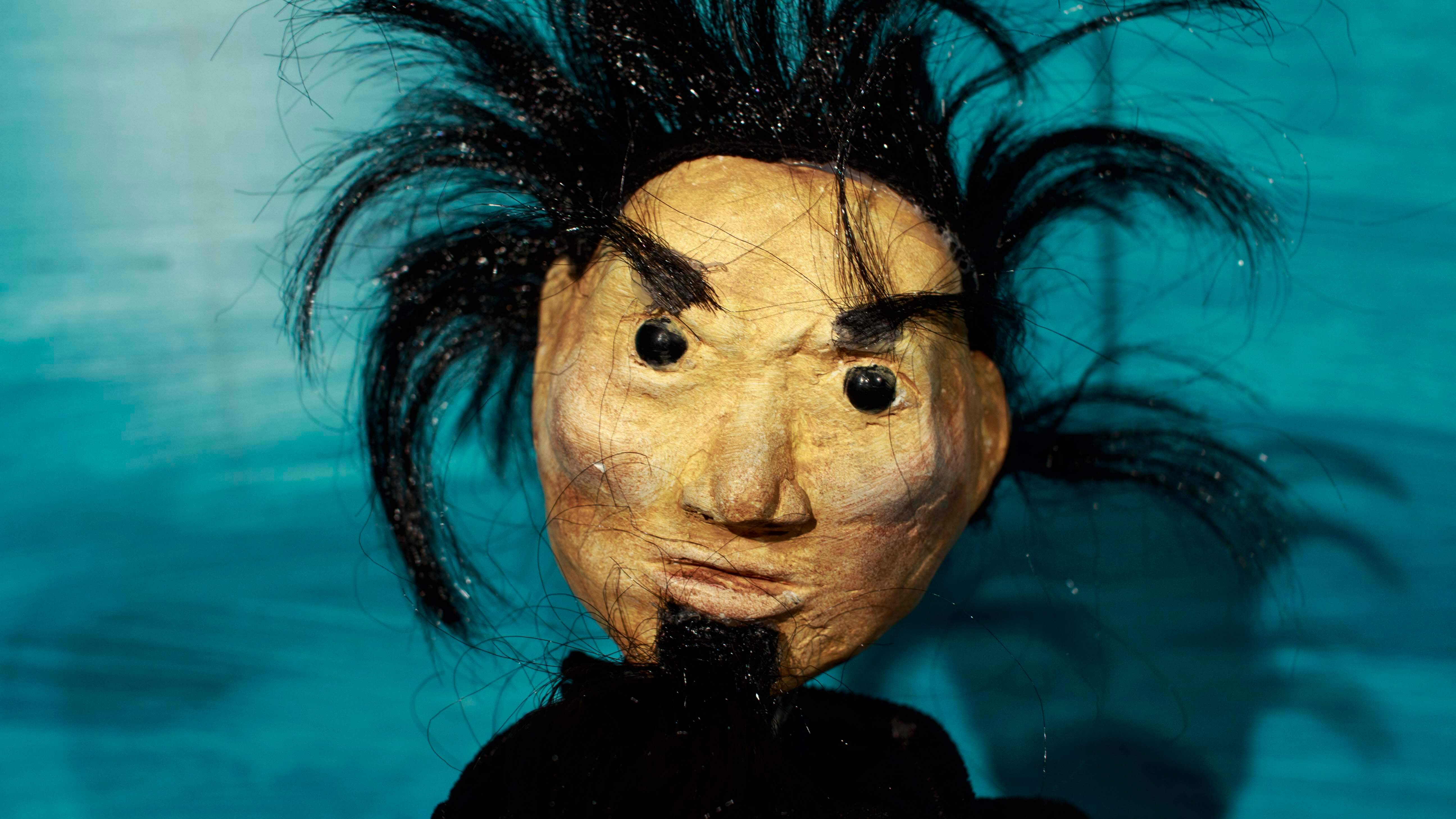 zbliżenie na twarz lalki przedstawiającej mężczyznę o czarnych sterczących włosach, z czarną brodą i czarnymi oczami, tło niebieskie, zdjęcie ze spektaklu dzielny kapitan ahab Teatru Gdynia Główna